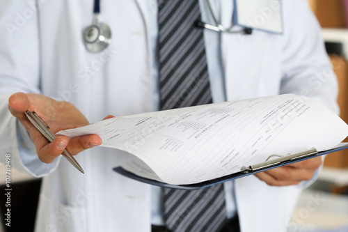 Male medicine doctor hand holding silver pen looking in clipboar photo