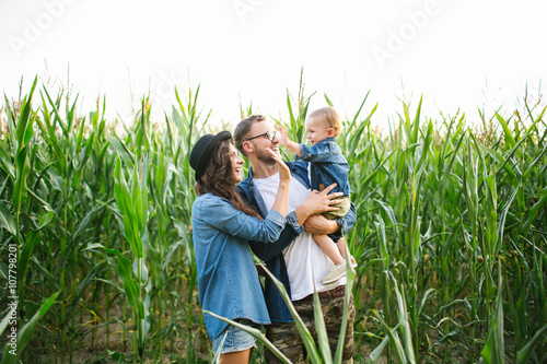Young hipster father mother holding cute baby in corn field