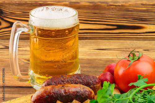 Grilled meat sausages with fried potatoes, fresh produce and mug of beer on wooden board
