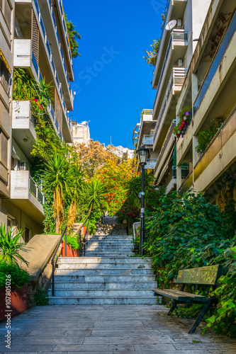 view of a narrow street leading to the top of lycabetus hill in athens with a long staircase surrounded by flowers.