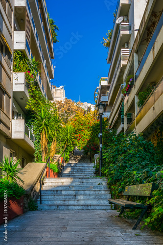 Fototapeta Naklejka Na Ścianę i Meble -  view of a narrow street leading to the top of lycabetus hill in athens with a long staircase surrounded by flowers.