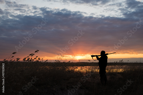 Photographie Silhouette du chasseur avec le fusil de chasse sur un coucher de soleil fond