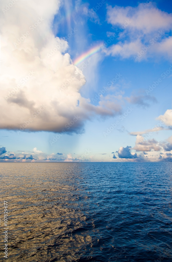 Blue ocean, light of large clouds reflected on surface, rainbow