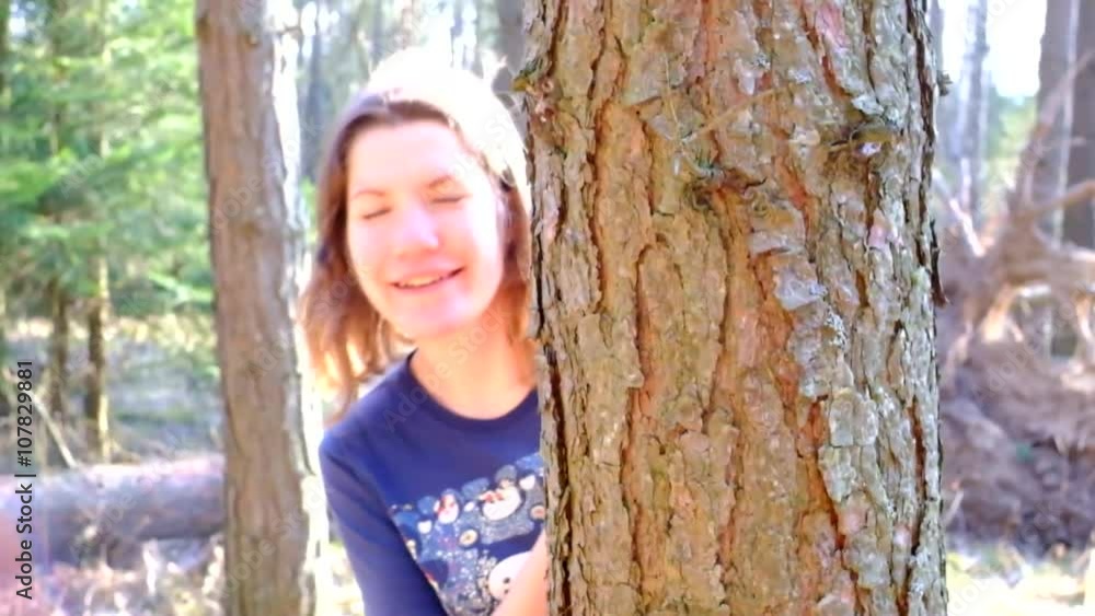 A girl looks out from behind a tree and smiling A girl looks out from behind a tree and smiling