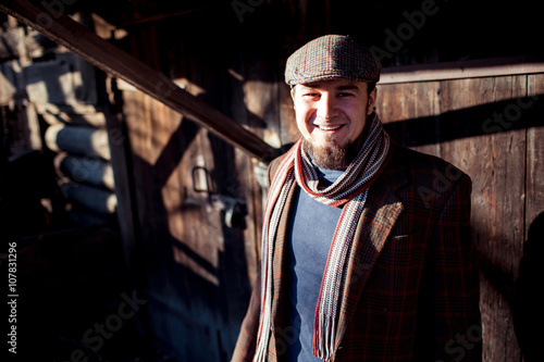 Man in flat cap with old-fashioned outfit outdoors on  background of wooden constructions.
