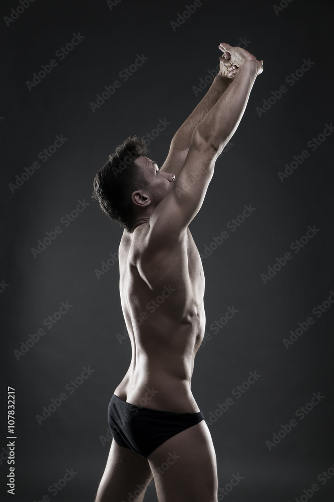 Naklejka premium Handsome muscular bodybuilder posing on gray background. Low key studio shot
