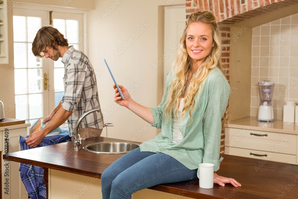 Pretty blonde using tablet while boyfriend ironing a shirt Pretty blonde using tablet while boyfriend ironing a shirt