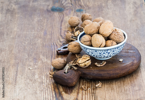 Walnuts in ceramic bowl and on cutting board with nutcracker over rustic wooden background
