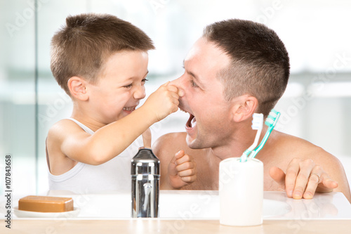 smiling child brushes his teeth with dad in the bathroom