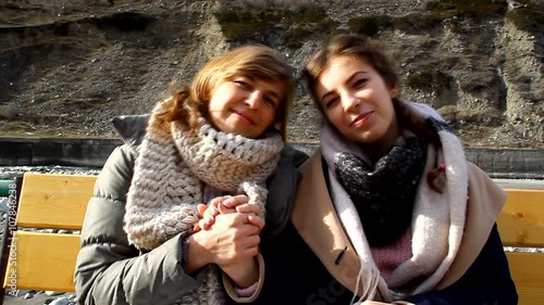 Mother and daughter sitting on a bench outdoors, talking, chatting, smiling