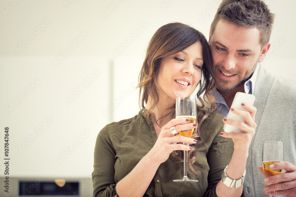 young casual couple cheers with champagne and phone in the kitchen young casual couple cheers with champagne and phone in the kitchen