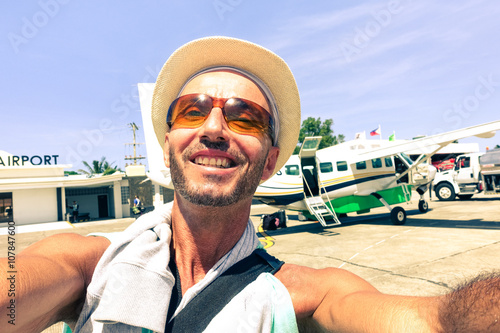 Cheerful traveler man selfie at airport with airplane background - Passenger tourist taking self photo after plane landed at Panay island  - Concept of joyful world travel and air transport trip photo