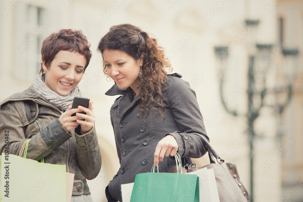 couple of women shop together with phone in cityscape couple of women shop together with phone in cityscape