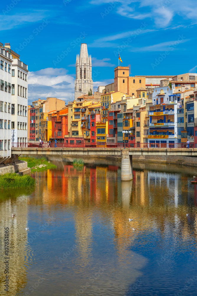 Church of Sant Feliu, colorful yellow and orange houses and bridge Pont de Sant Agusti reflected in water river Onyar, in Girona, Catalonia, Spain