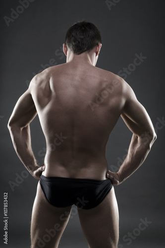 Handsome muscular bodybuilder posing on gray background. Low key studio shot © staras