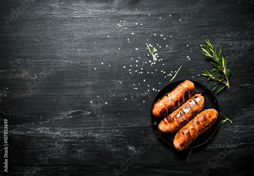 Photo Fried sausages in a pan with rosemary .