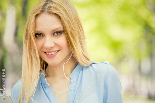 smiling blonde young woman with phone portrait in a green cityscape