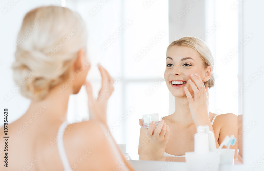 happy woman applying cream to face at bathroom happy woman applying cream to face at bathroom
