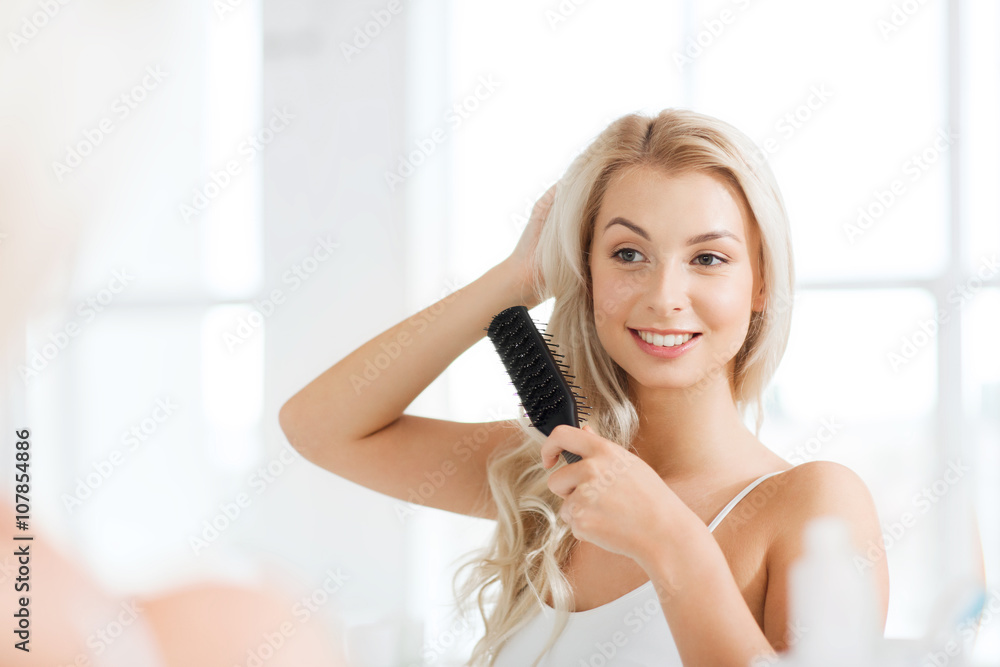 Fototapeta premium happy woman brushing hair with comb at bathroom