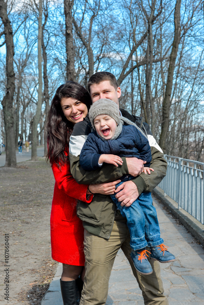 Portrait of happy young family spending time together in green nature in park. Mother, father and son having fun outdoors on a spring sunny day. Concept of happy family life, love and happiness. Portrait of happy young family spending time together in green nature in park. Mother, father and son having fun outdoors on a spring sunny day. Concept of happy family life, love and happiness.