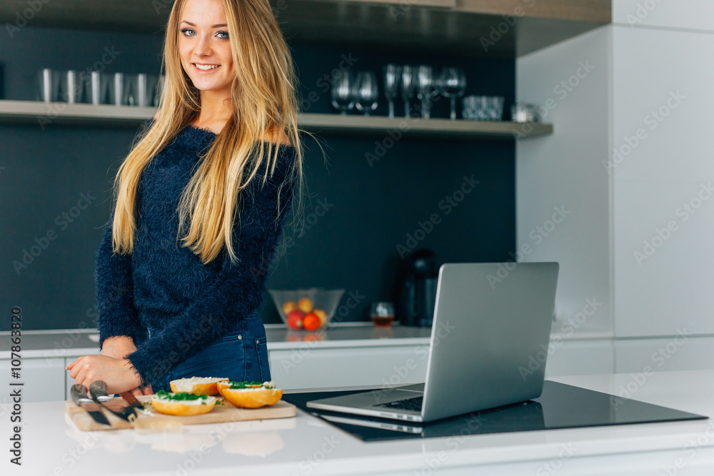 Young girl making sandwiches in the kitchen. Laptop on the kitchen table Young girl making sandwiches in the kitchen. Laptop on the kitchen table