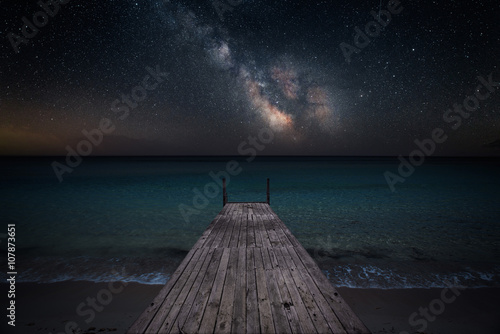 Fotografia Milky way over che seashore and small wooden jetty in perspective