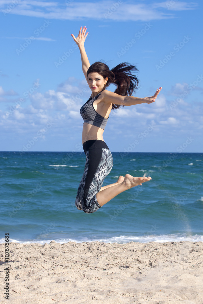 Pretty woman jumping with excitement on a beach with ocean in the background Pretty woman jumping with excitement on a beach with ocean in the background