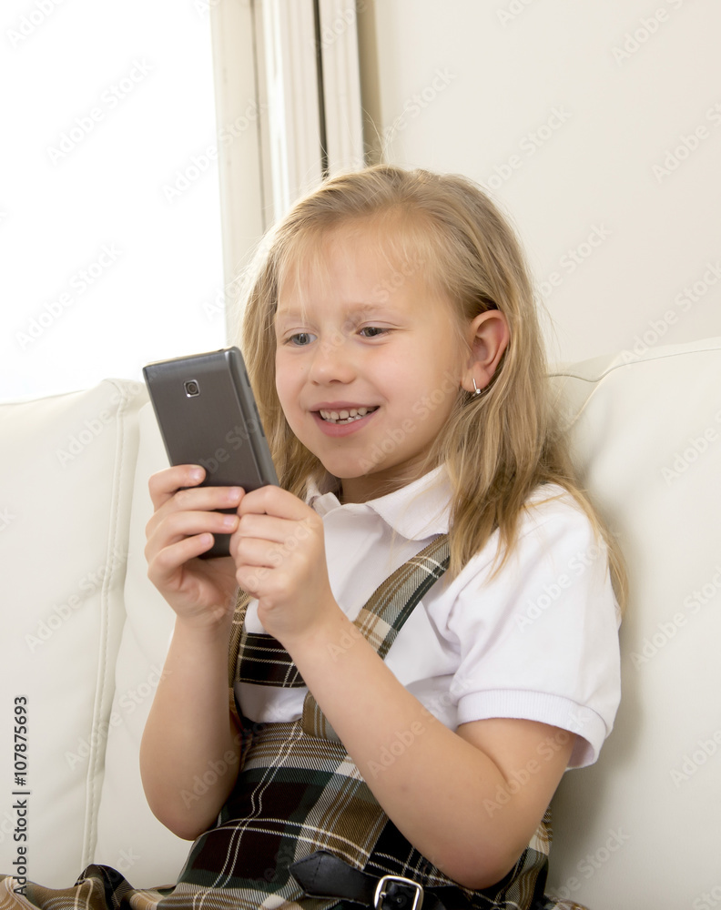 female child with blond hair sitting on couch using internet app on mobile phone female child with blond hair sitting on couch using internet app on mobile phone