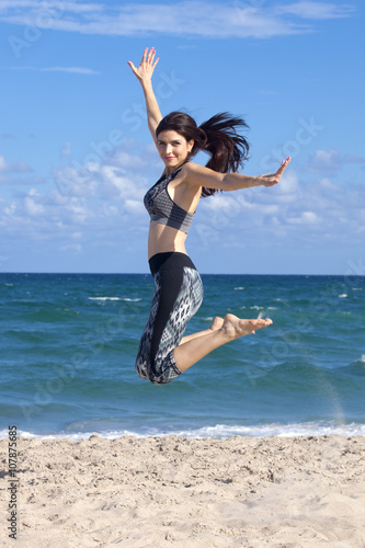 Pretty woman jumping with excitement on a beach with ocean in the background
