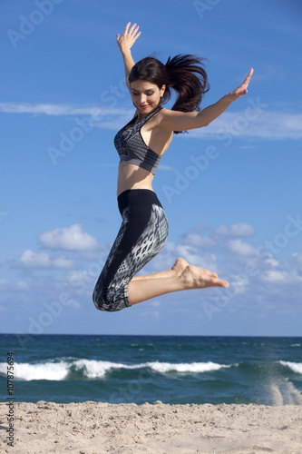 Pretty woman jumping with excitement on a beach with ocean in the background