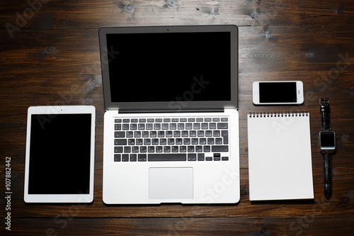 Top view office. On a wooden table lay a tablet computer, a laptop, a phone, a tablet, watch
