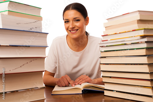 Excited woman reading behind the table between two pile of books