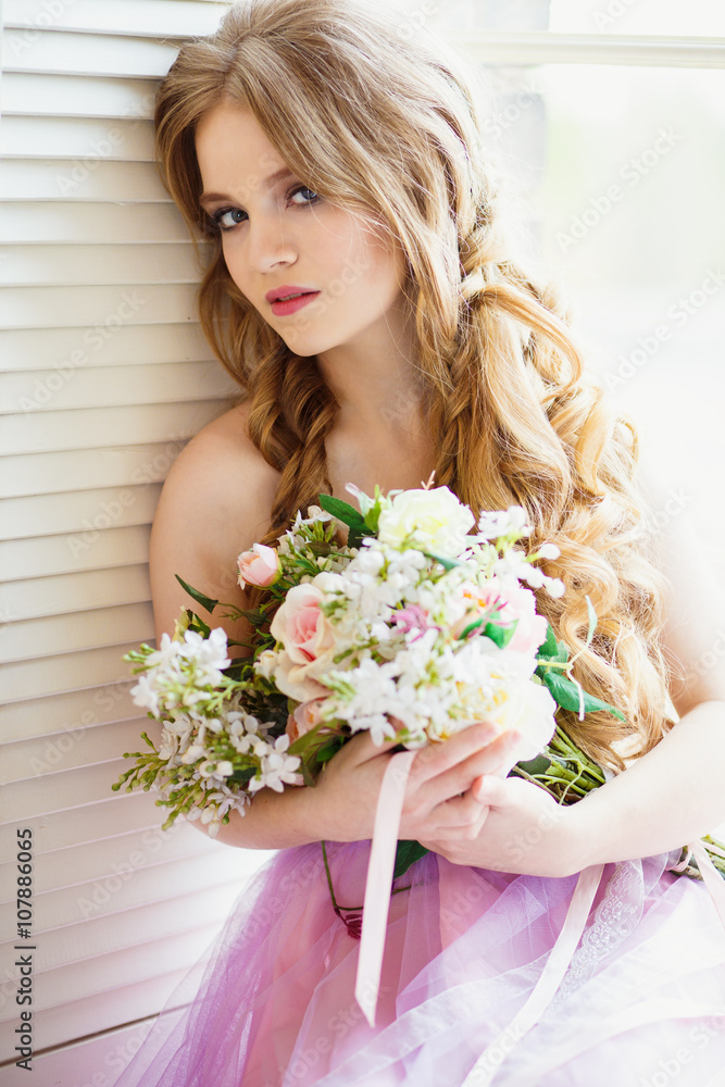 Portrait of pretty young girl in a sweet dress and long blonde hair sitting on a window with flowers composition