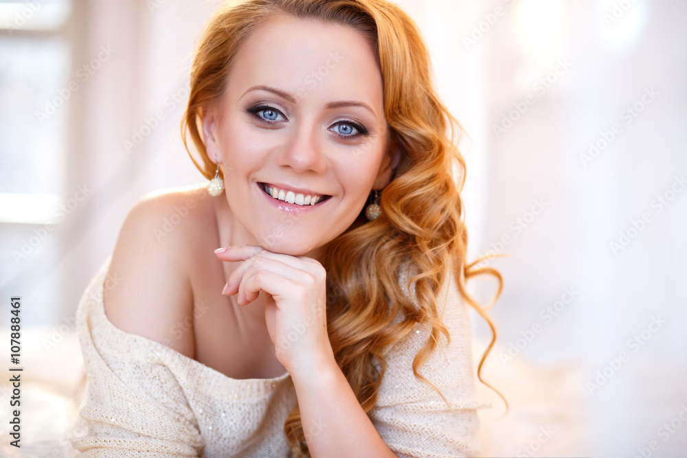 Young beautiful woman in a warm pullover in a light bedroom in a morning. Close up portrait, blue eyes and natural makeup