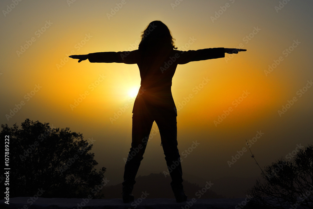 woman with arms raised at sunset