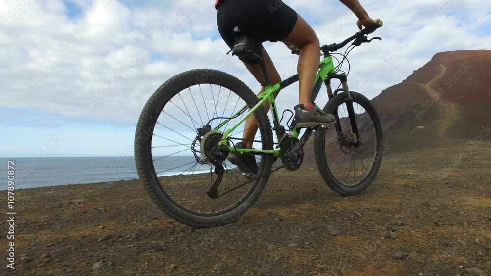 Woman cycling riding bicycle on mountain by sea on mountain bike. Sporty woman cyclist biking in nature. Active fitness girl living healthy lifestyle. ACTION CAMERA, Lanzarote, Canary Islands, Spain. Woman cycling riding bicycle on mountain by sea on mountain bike. Sporty woman cyclist biking in nature. Active fitness girl living healthy lifestyle. ACTION CAMERA, Lanzarote, Canary Islands, Spain.
