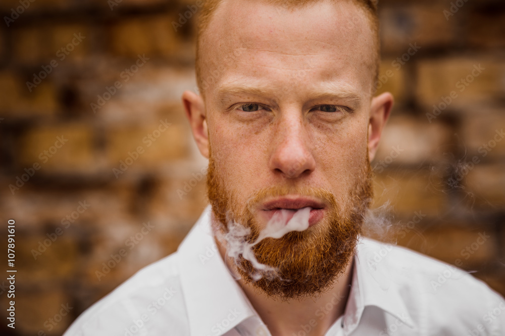 Fototapeta premium portrait of smoking young red hair man with beard