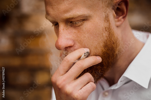 portrait of smoking young red hair man with beard photo