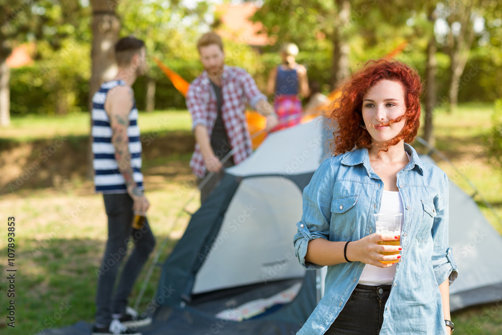 Ginger female with glass of beer stands in youth camp