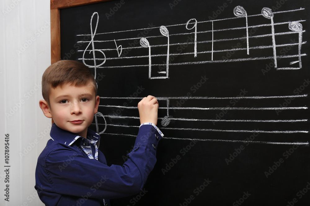 Cute boy writing at the blackboard with musical notes, in the classroom Cute boy writing at the blackboard with musical notes, in the classroom