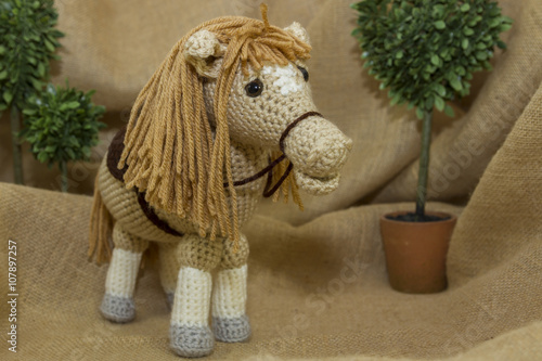 A handcrafted crochet toy horse photographed on a rustic burlap backdrop.