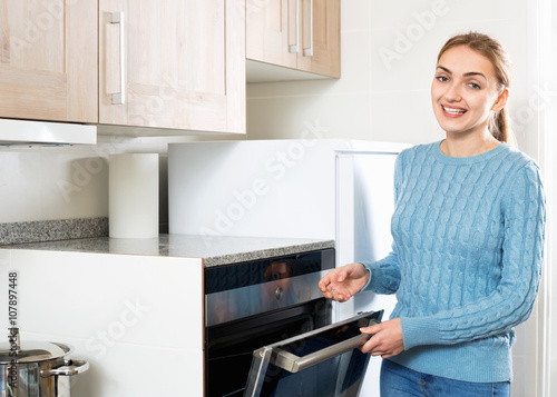 Smiling young housewife warming up electric oven