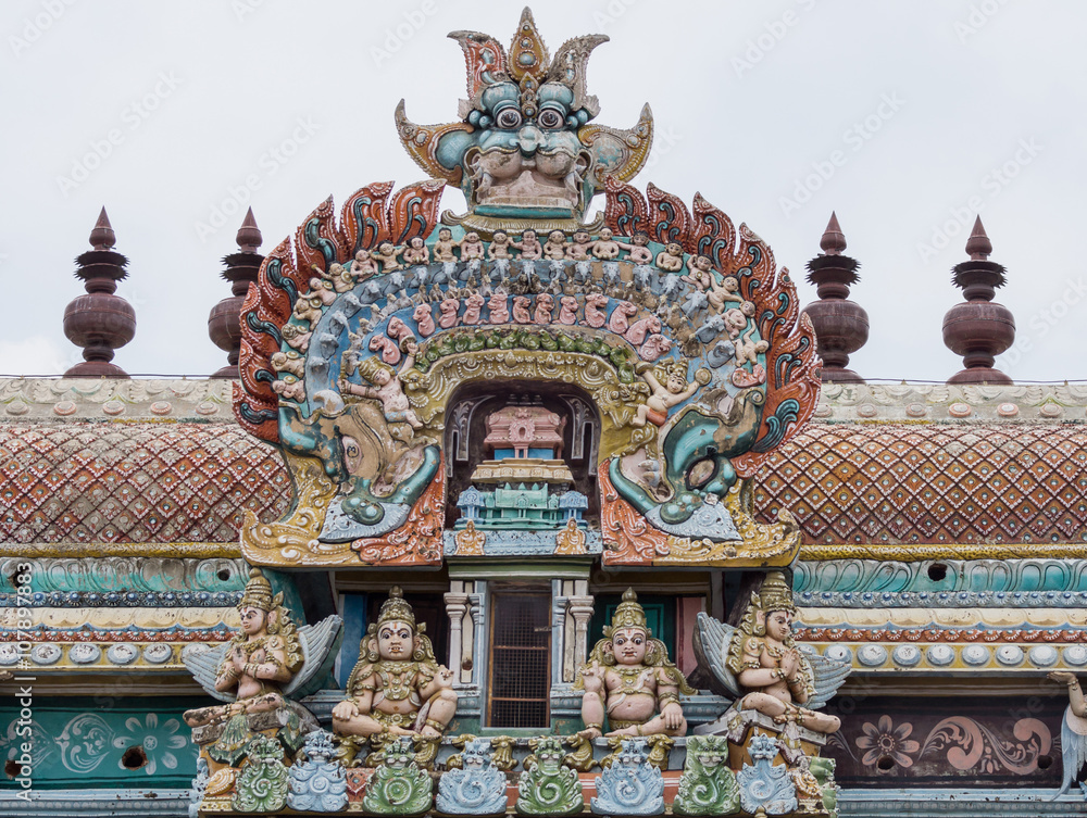 Trichy, India - October 15, 2013: Closeup of bow decoration on the Vimanam of one Gopuram at Shirangam temple. Monster face on top of bow showing small humans, elephants, horses, parrots, dogs Trichy, India - October 15, 2013: Closeup of bow decoration on the Vimanam of one Gopuram at Shirangam temple. Monster face on top of bow showing small humans, elephants, horses, parrots, dogs