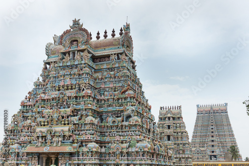 Trichy, India - October 15, 2013: Three of the twenty-one gopurams in a row at the Shirangam Vishnu temple. Hundreds of statues. Pastel colors against a gray sky which is broken open by blues.
