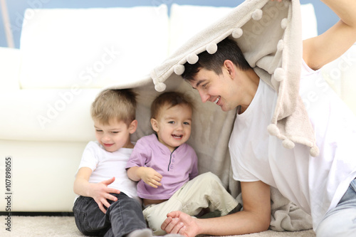 Family concept. Father with sons are playing under blanket in the room