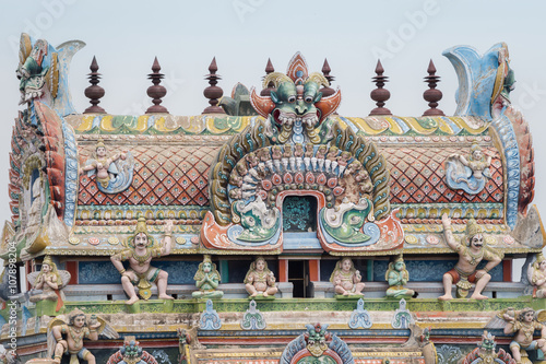 Trichy, India - October 15, 2013: Closeup of the top of the gopuram, called Vimanam, shaped as a cake, with plenty of statues in pastel colors. Garudas on corners. photo