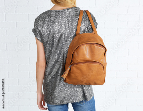 Back of woman with brown leather backpack against white brick wall background