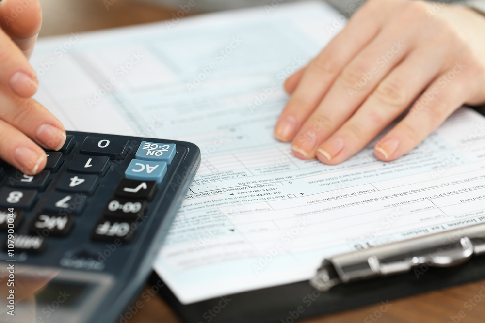 Female hand holding a pen and using calculator while filling in the individual income tax return, close up Female hand holding a pen and using calculator while filling in the individual income tax return, close up