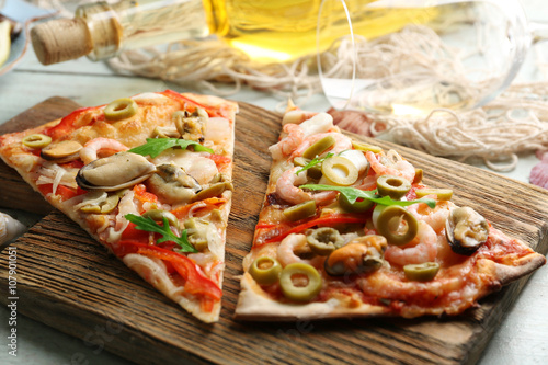 Pizza slices with seafood, red pepper, green olives and bottle of wine on wooden table