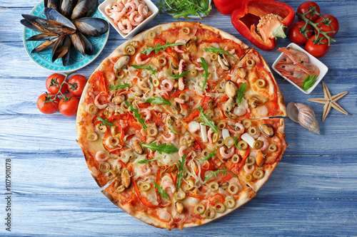 Pizza with seafood, red pepper and green olives on blue wooden table